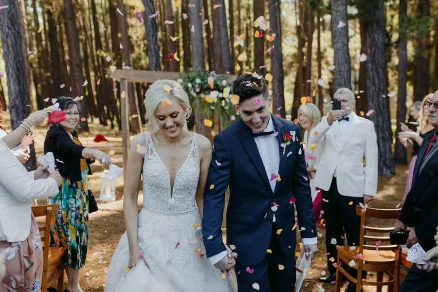 Bride and groom walking through colourful petals at a forest ceremony.