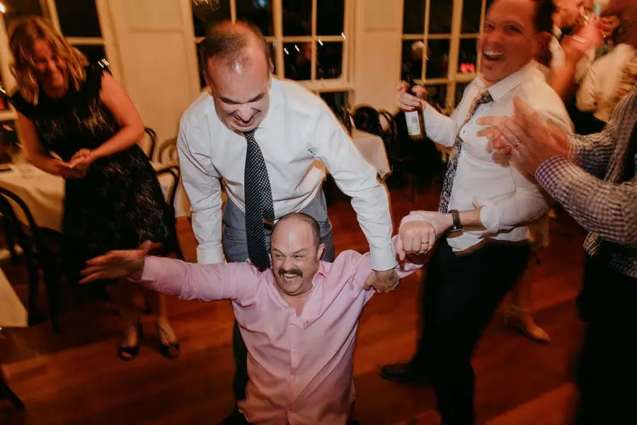 Men helping a laughing guest rise from the dance floor.