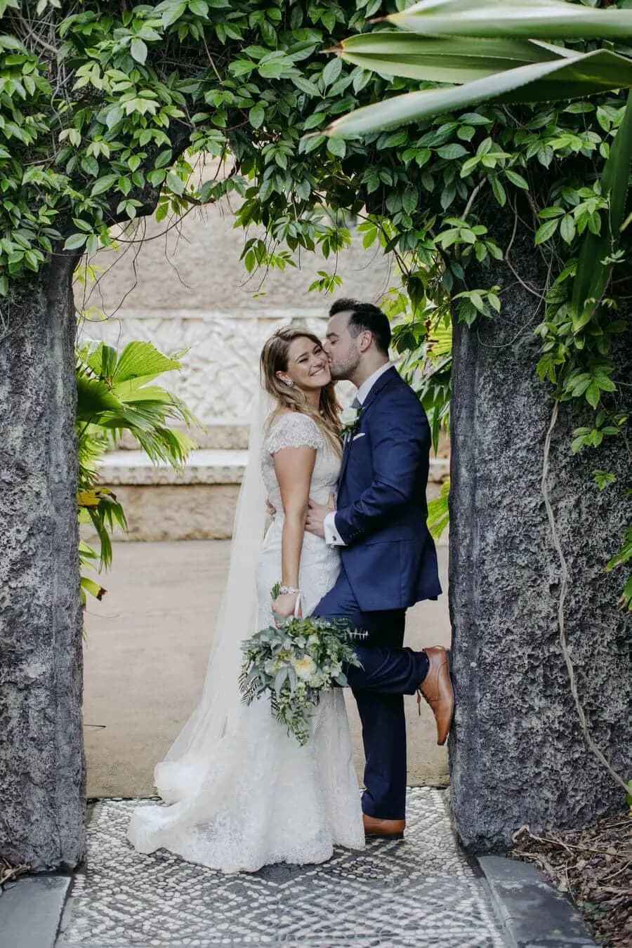 Groom lifting the bride beside an ivy-covered garden doorway.