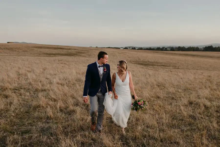 Bride and groom walking together across a dry golden field.