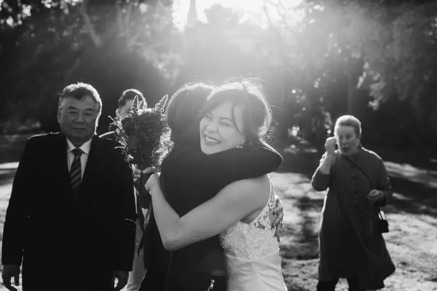 Black-and-white photograph of a woman embracing a guest in bright backlighting.