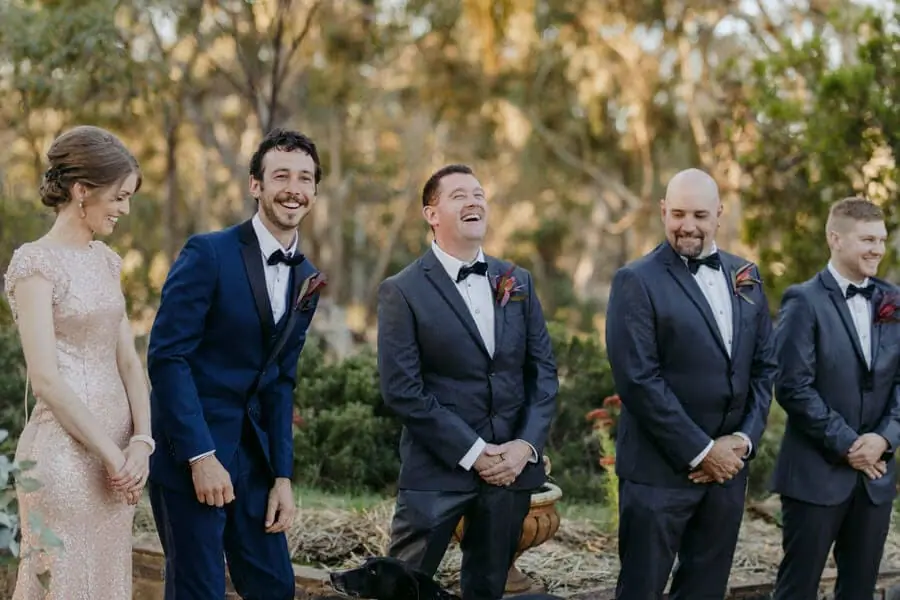 Groom and companions laughing together at a woodland ceremony.