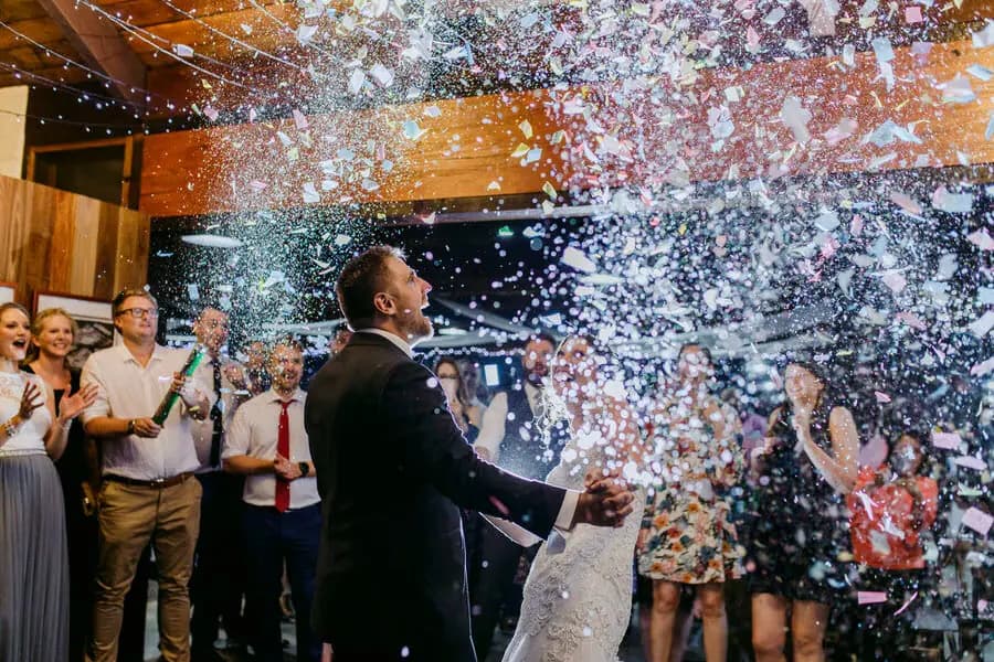 Bride and groom reacting beneath a burst of confetti at the reception.