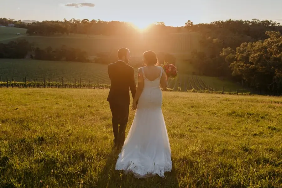 Couple walking across a sunlit hillside toward the setting sun.