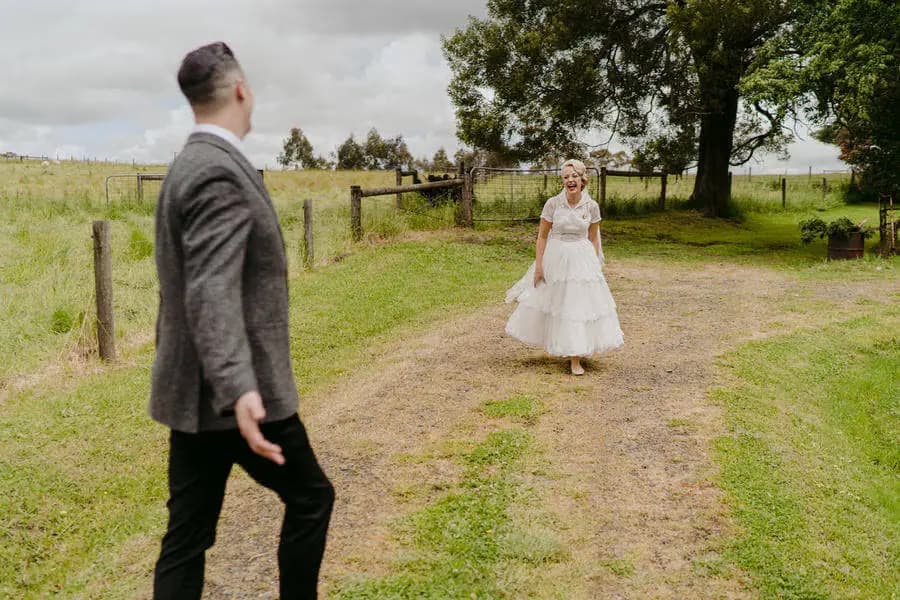 Groom spreading his arms as the bride approaches across a field.