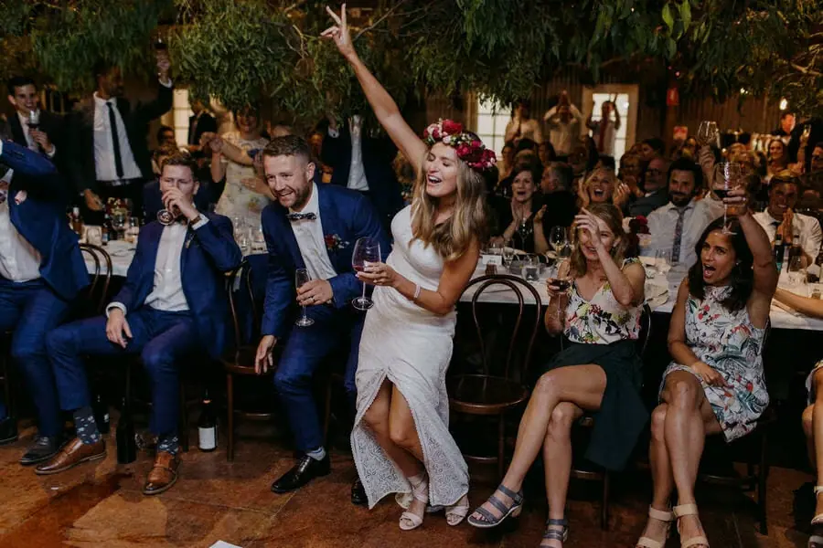 Woman raising an arm while cheering guests sit around her.