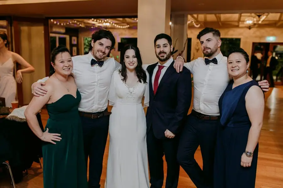 Bride and guests posing together with arms around each other inside a reception.