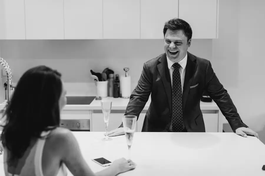 Black-and-white photograph of a suited man smiling across a kitchen island.