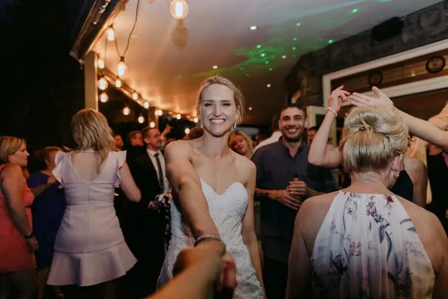 Bride smiling and dancing with guests beneath reception lights.