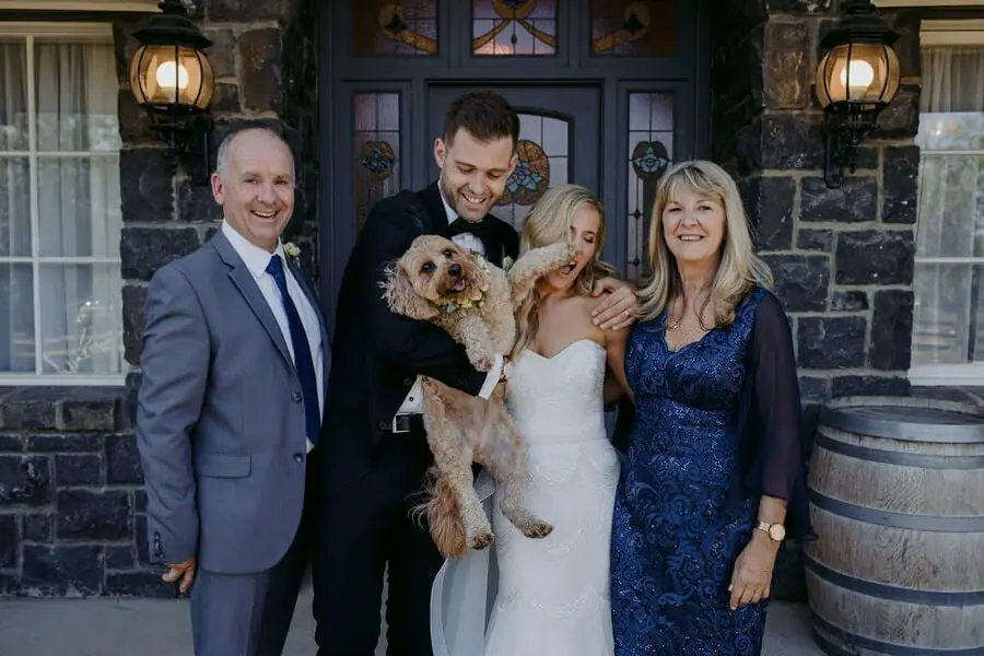 Couple posing with two guests and a small dog outside a stone building.