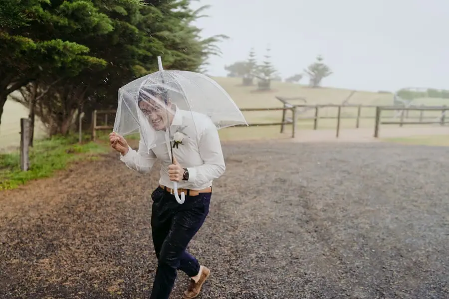 Man walking under a clear umbrella on a wet gravel path.
