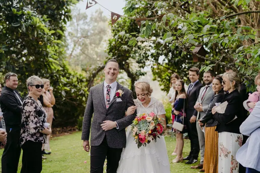 Bride walking arm in arm with a man between garden ceremony guests.