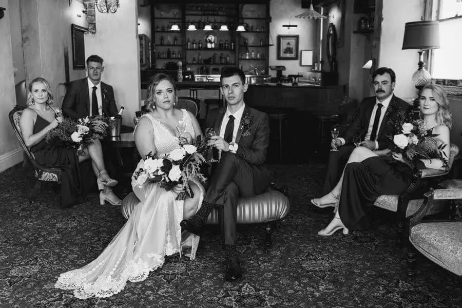 Black-and-white photograph of wedding party members seated in an ornate room.
