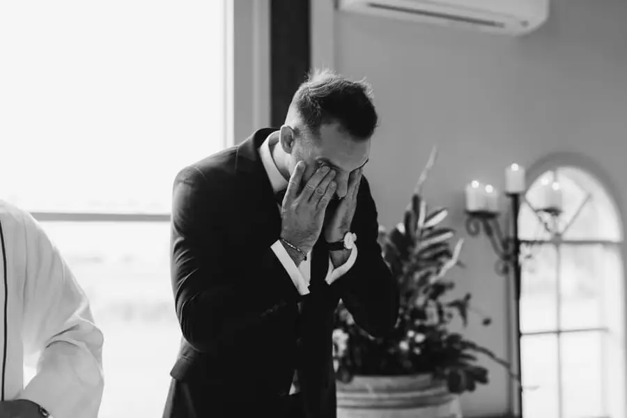 Black-and-white photograph of a suited man covering his face with both hands.