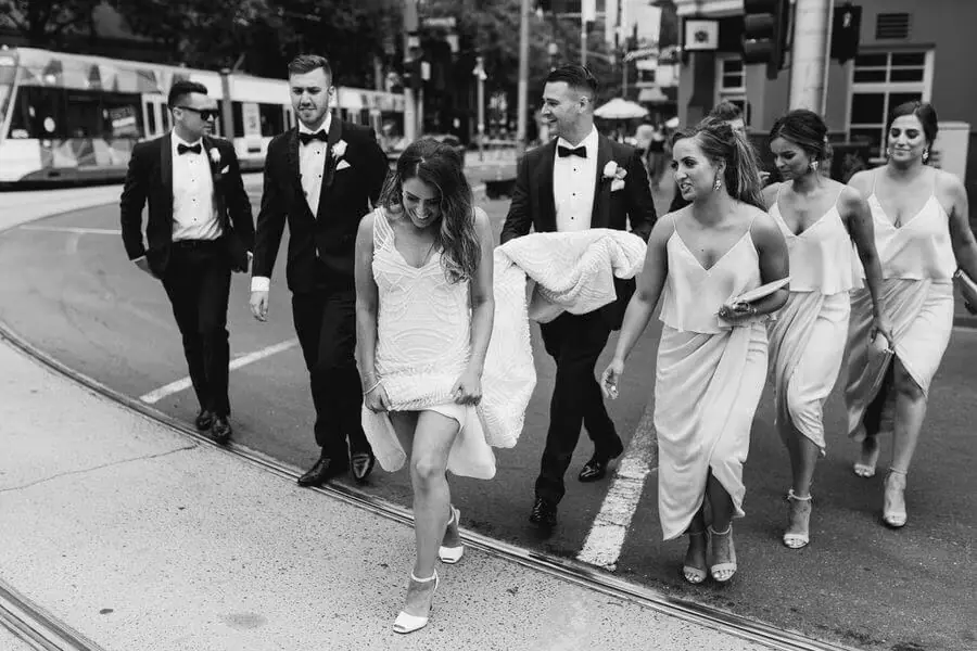 Black-and-white photograph of a wedding party walking through a city street.