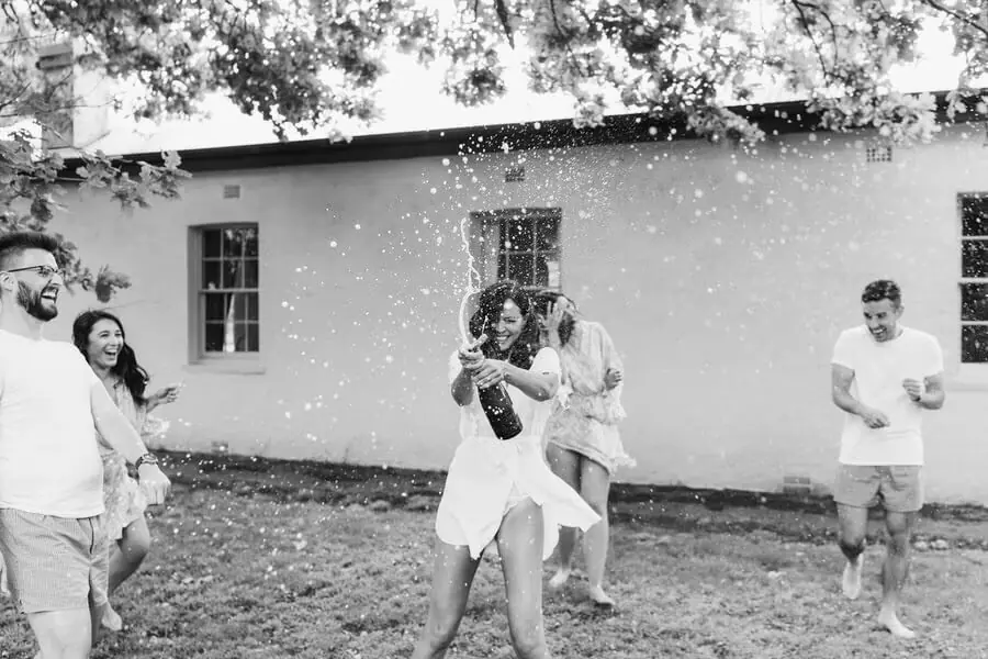 Black-and-white photograph of a woman spraying sparkling wine outside.