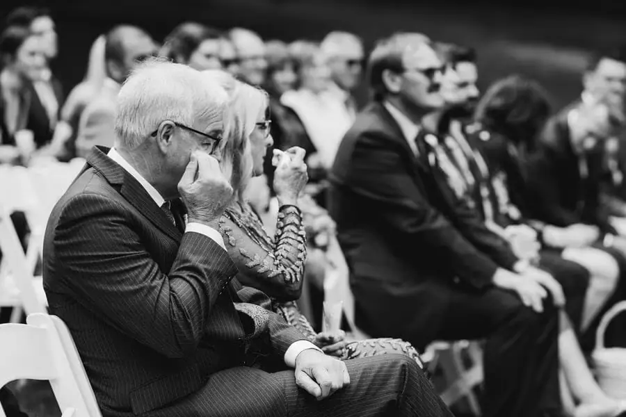 Black-and-white photograph of seated guests, including an older man touching his face.