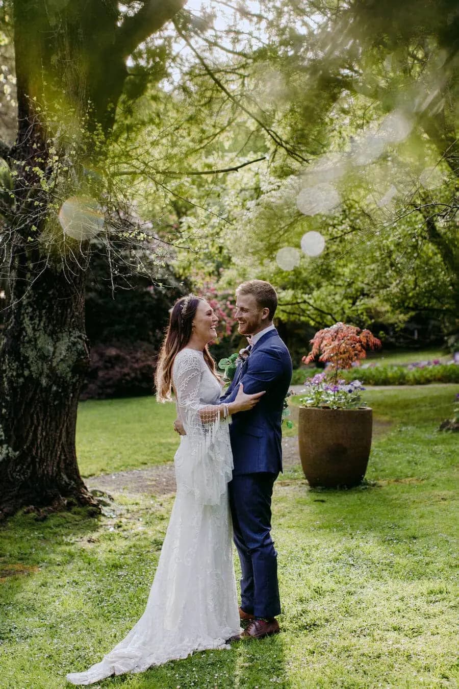 Couple holding hands beneath trees and hanging white decorations.