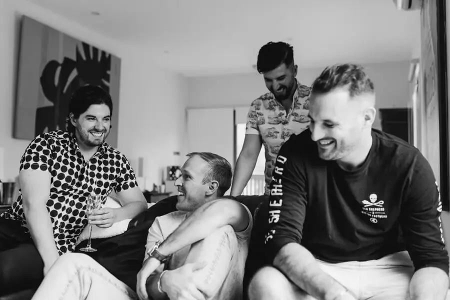 Black-and-white photograph of men laughing during preparations indoors.