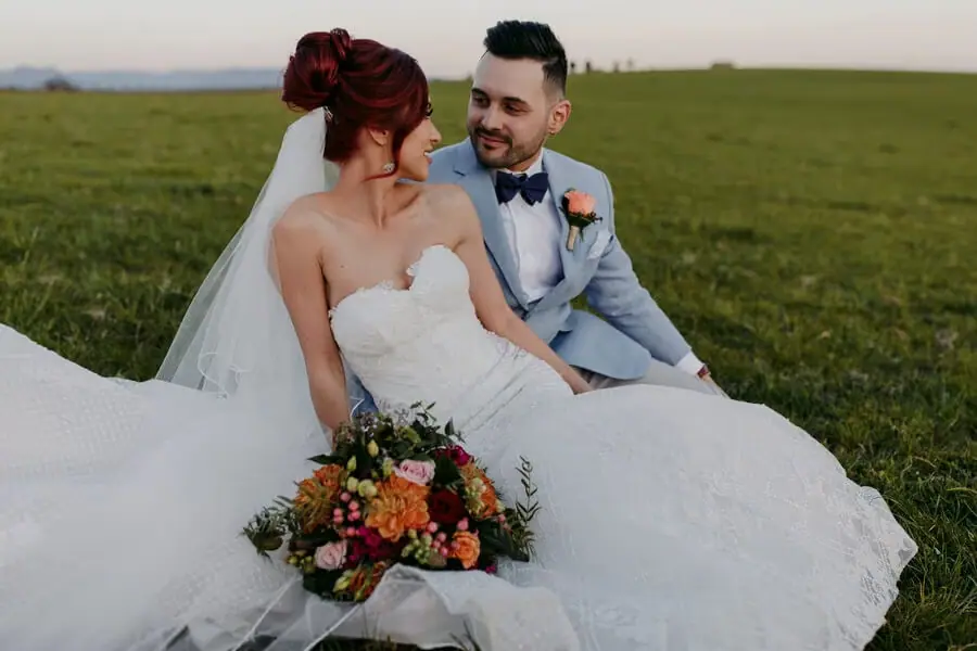 Bride and groom sitting together on a lawn with a colourful bouquet.