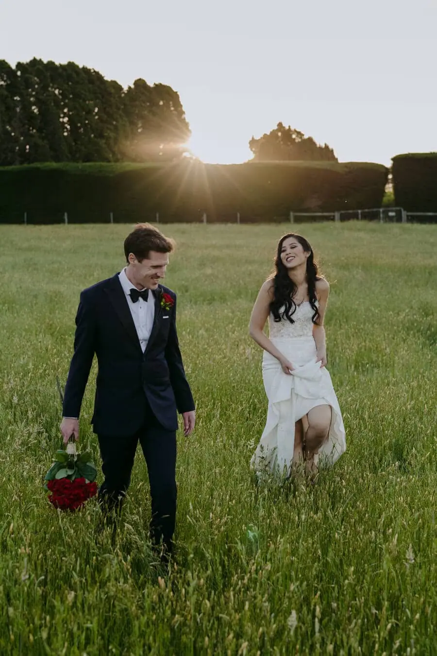 Couple walking through a grassy field at sunset.