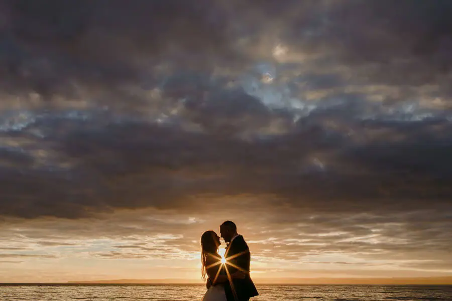 Couple silhouetted against a golden seaside sunset.