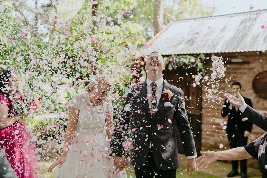Bride and groom laughing beneath a shower of colourful confetti.