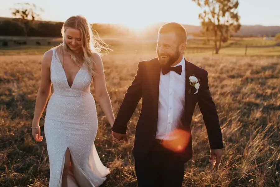 Bride and groom walking through a golden field at sunset.