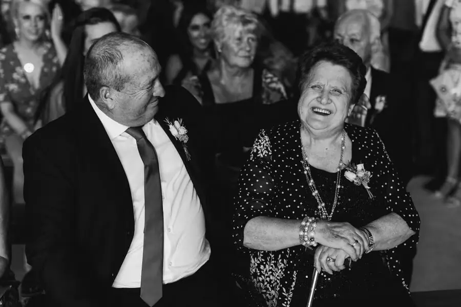 Black-and-white photograph of an older couple laughing among guests.