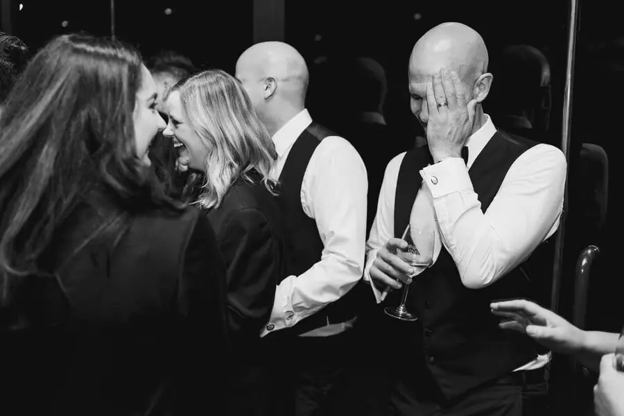 Black-and-white photograph of guests laughing and chatting at a reception.