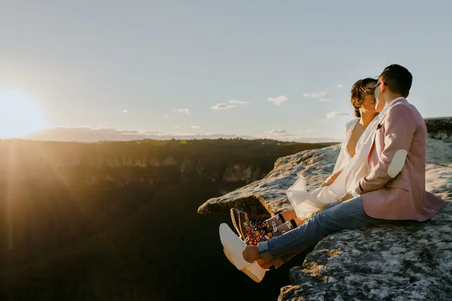 Couple sitting on a rocky ledge overlooking a sunlit valley.
