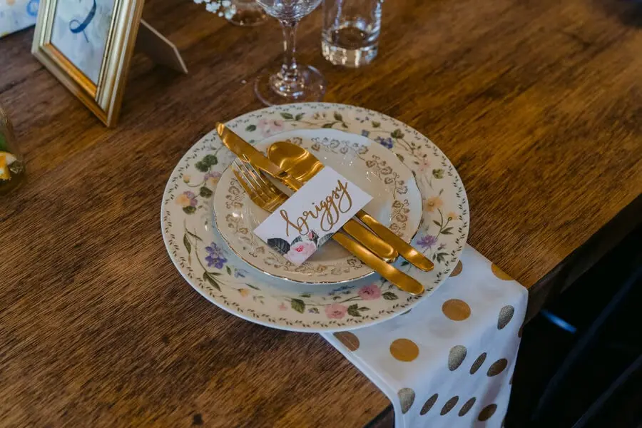 Decorated plate with gold cutlery and a handwritten place card on a wooden table.