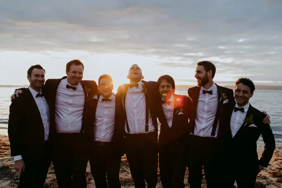 Men posing arm in arm near the sea at sunset.