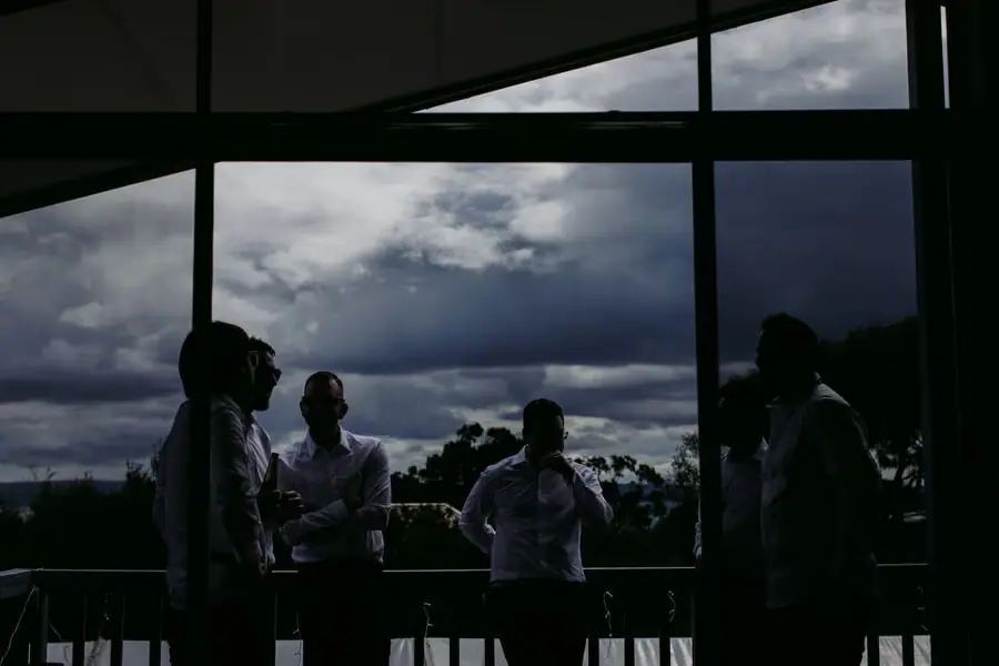Silhouetted men gathered beside wide windows beneath storm clouds.