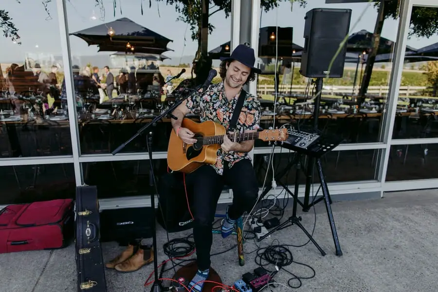 Guitarist singing into a microphone outside a glass reception building.