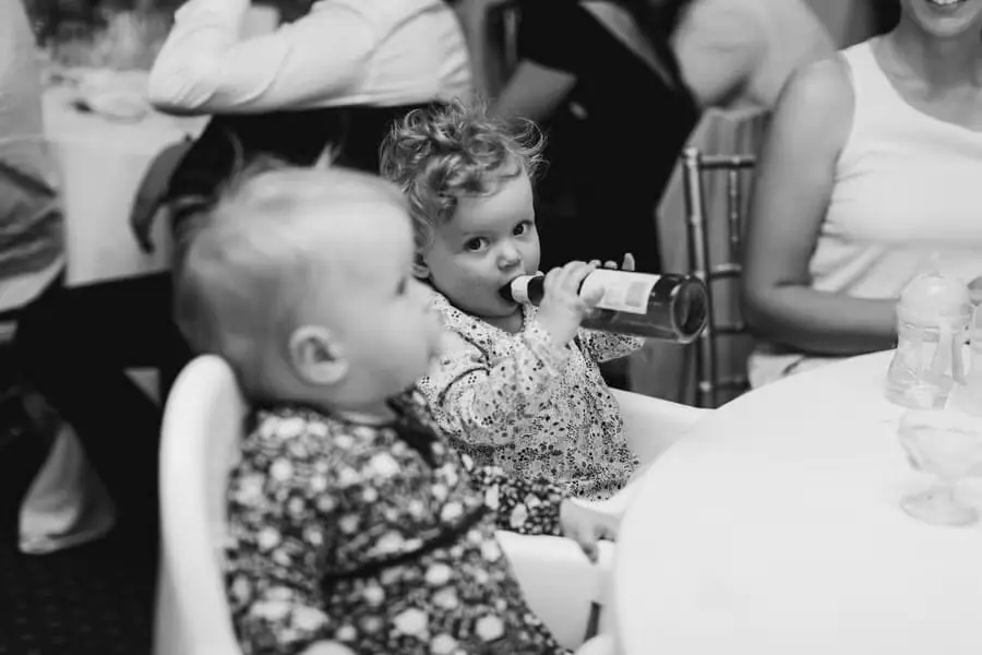 Black-and-white photograph of two children seated at a table, one drinking from a bottle.
