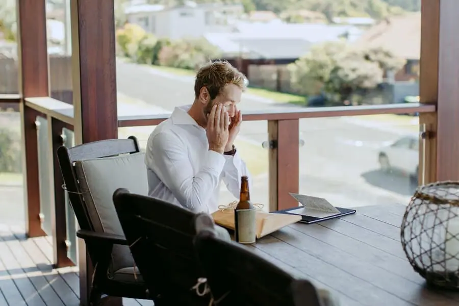 Man seated at an outdoor table covering his face with one hand.
