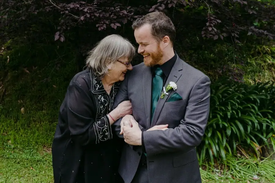 Man in a grey suit smiling and leaning close to an older woman in a garden.