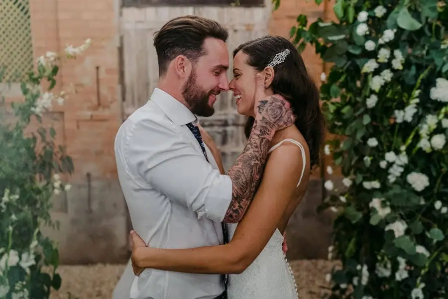 Couple embracing beside an ivy-covered brick wall.