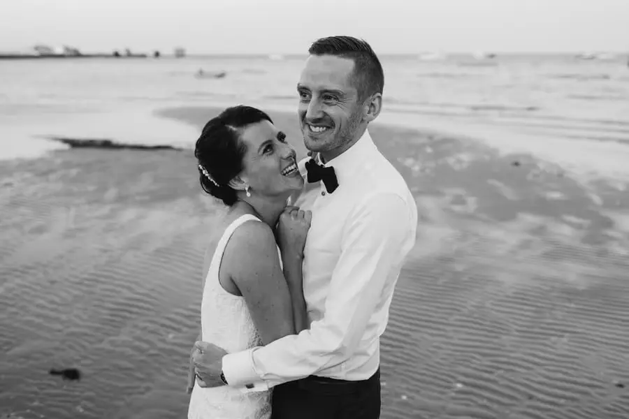 Black-and-white portrait of a couple embracing on a beach.