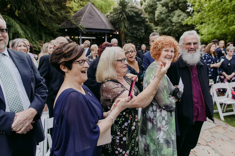 Guests applauding and laughing beside a garden ceremony.
