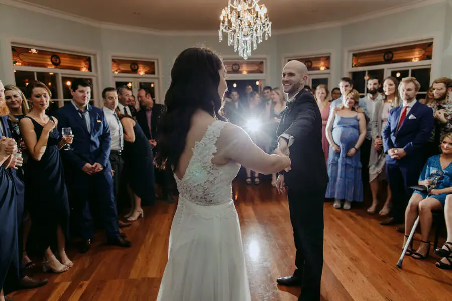 Bride and groom dancing before guests in a bright reception room.