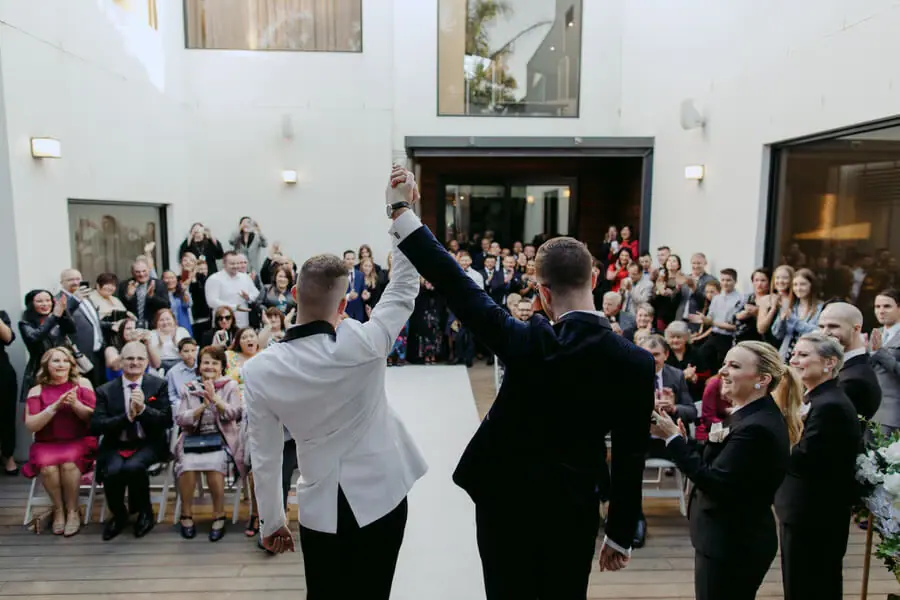 Two men raising their joined hands before applauding guests indoors.