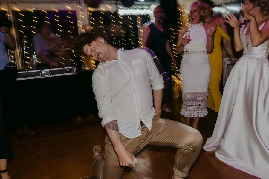 Man leaning back and dancing among cheering reception guests.