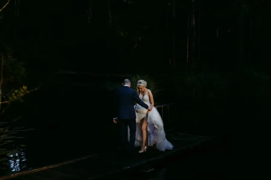 Couple embracing beside water in a dark forest.