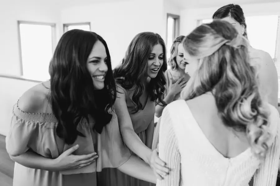 Black-and-white photograph of women smiling at the bride during preparations.