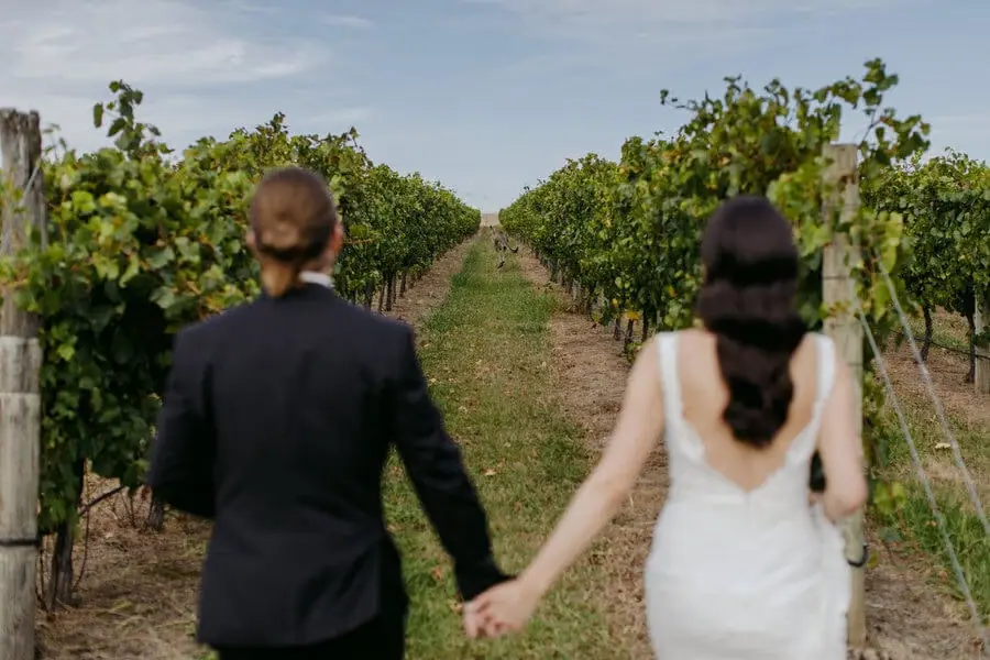 Couple walking hand in hand between vineyard rows.