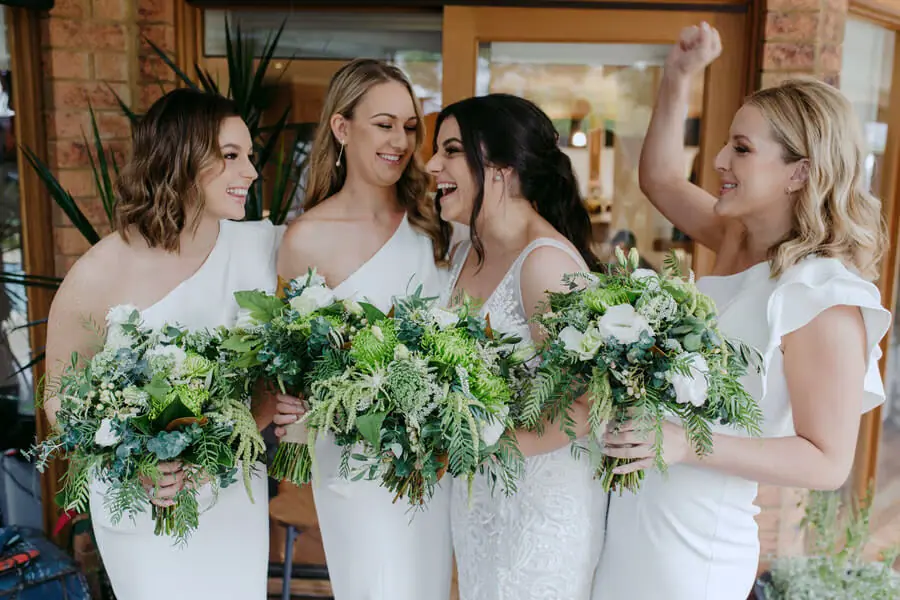 Bride and three women holding green and white bouquets and laughing together.