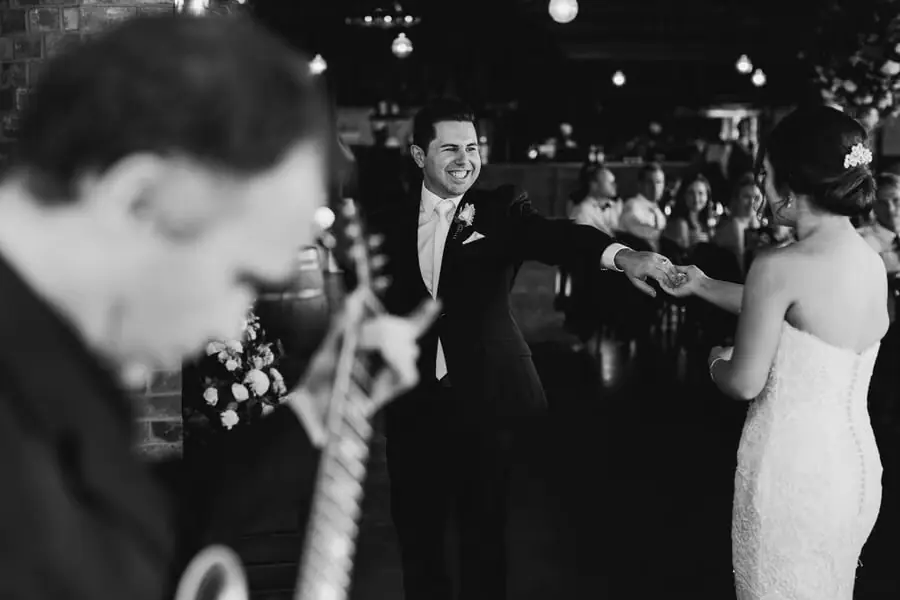 Black-and-white photograph of a groom holding the bride's hand on a dance floor.