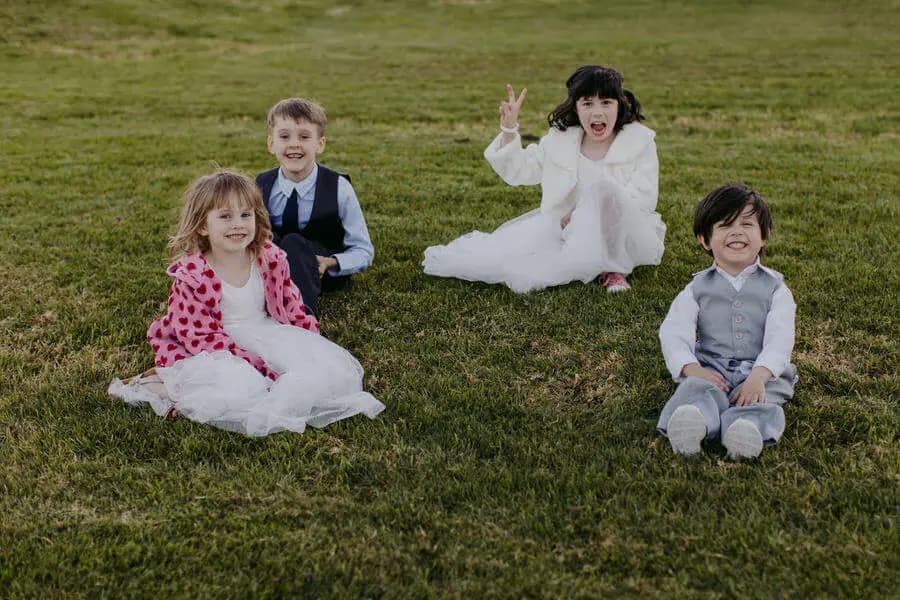 Four children smiling while sitting on a lawn.